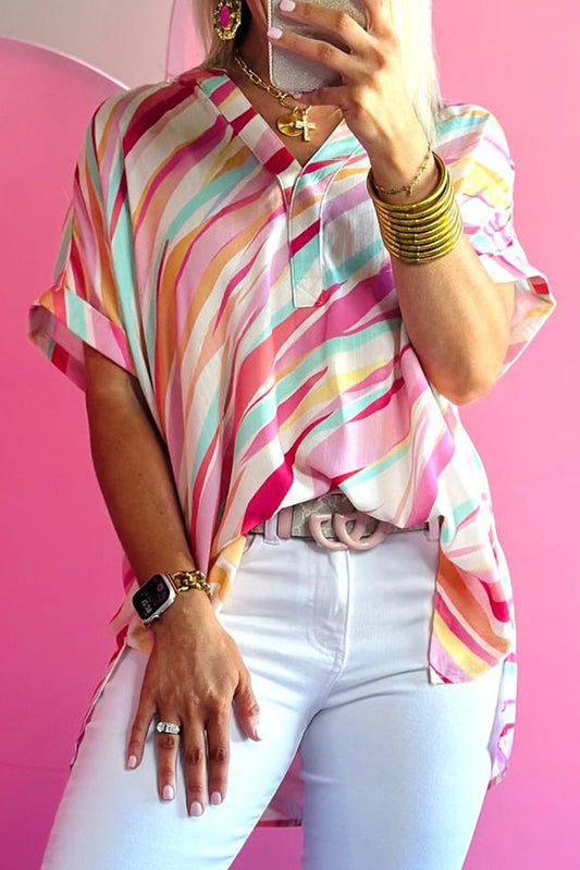 Person wearing a colorful striped shirt and white pants against a pink background