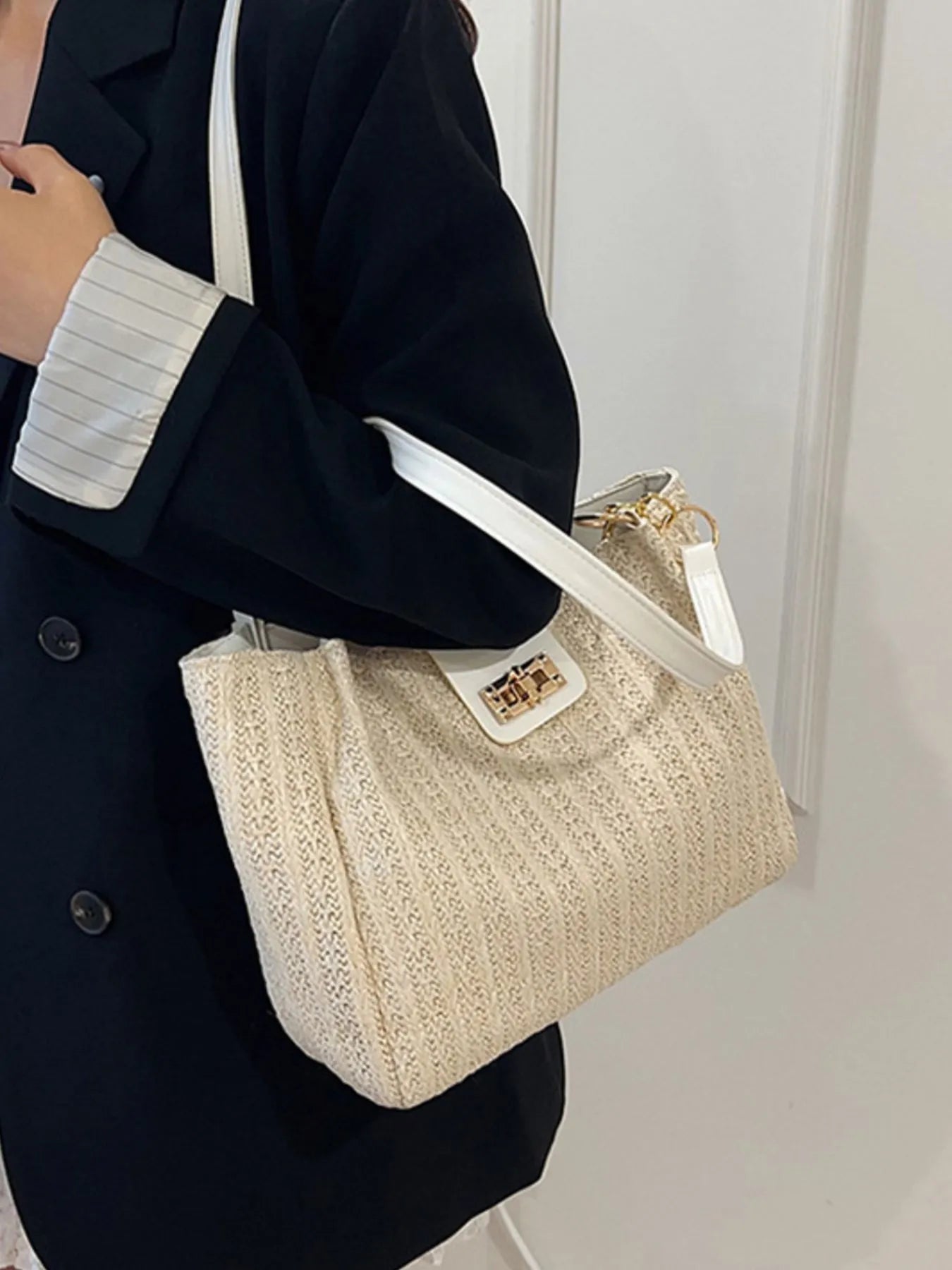 Person holding a beige handbag with a white strap against a plain background