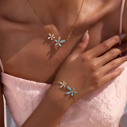 Woman wearing a gold necklace and bracelet with floral designs on a neutral background