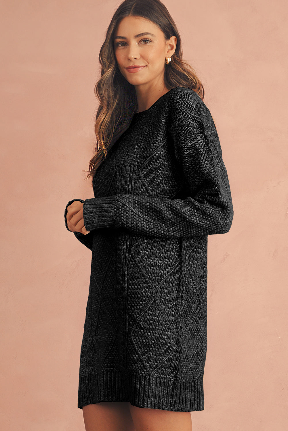 Woman wearing a black cable knit sweater dress against a beige background