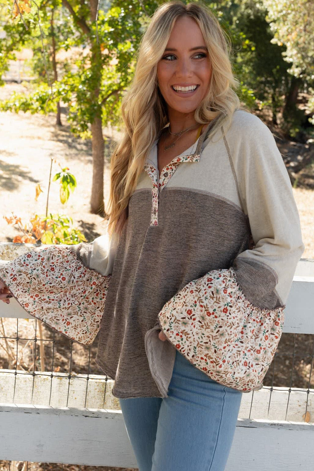 Woman wearing a two-tone sweater with floral sleeves and pocket, standing outdoors.