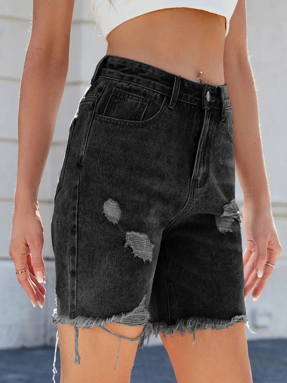 Black distressed denim shorts worn by a person against a neutral background
