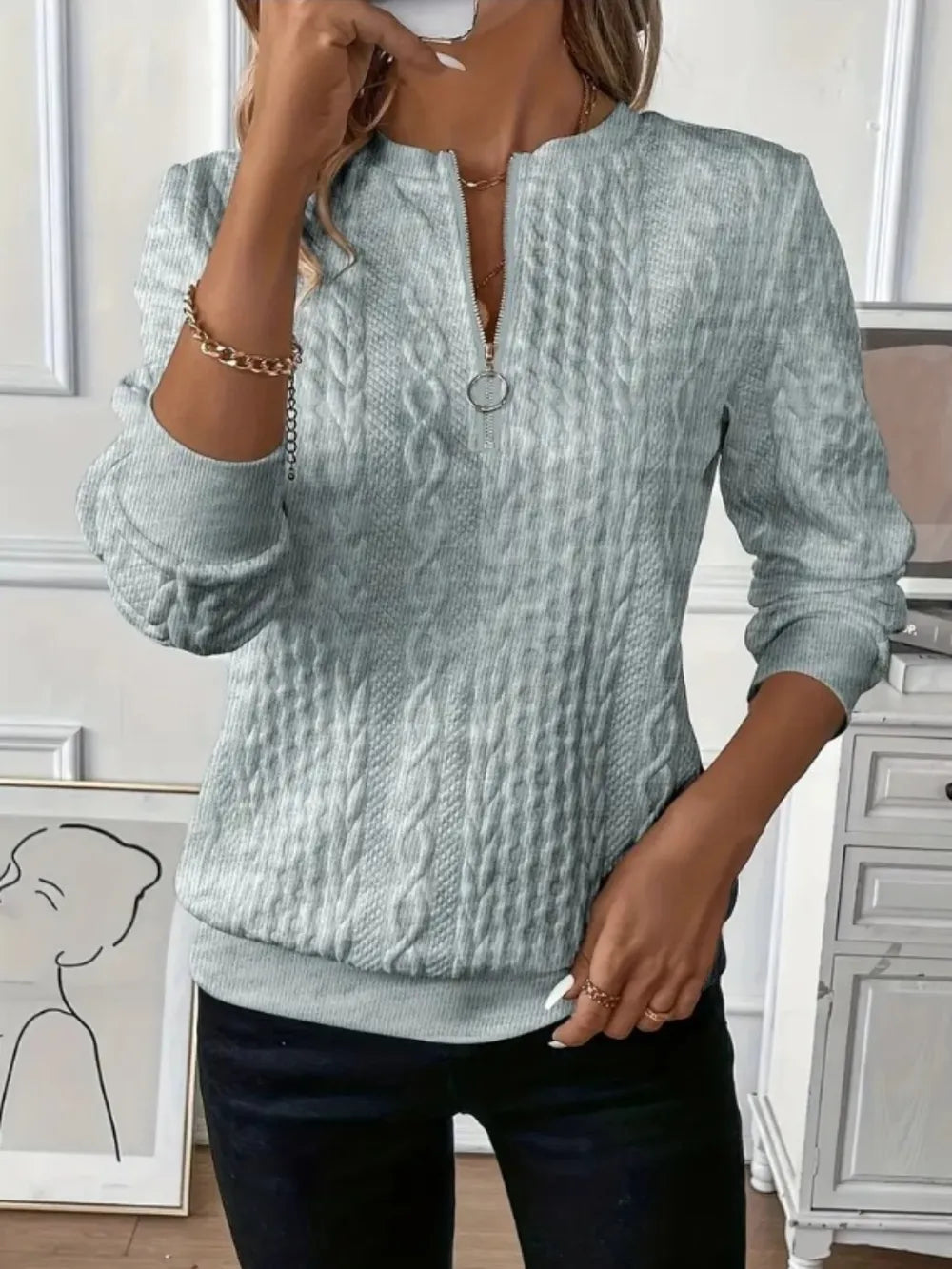 Person wearing a light blue cable knit sweater in an indoor setting.