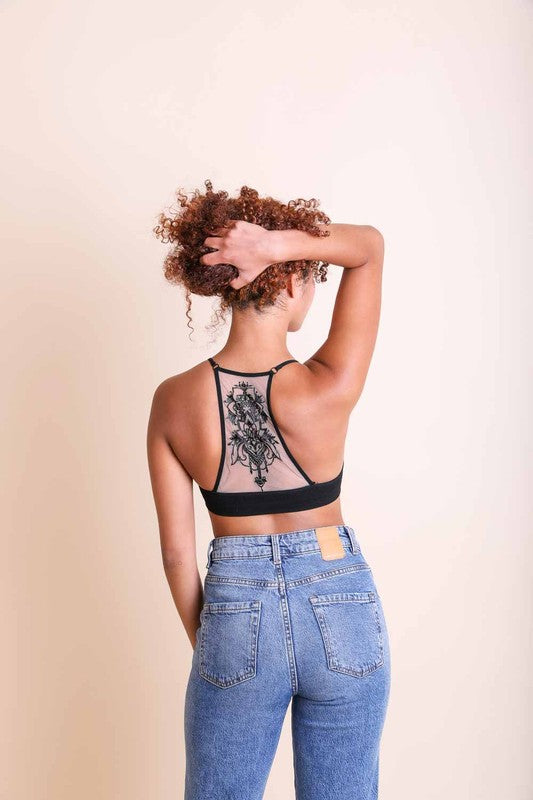 Person wearing a black lace top and blue jeans against a beige background