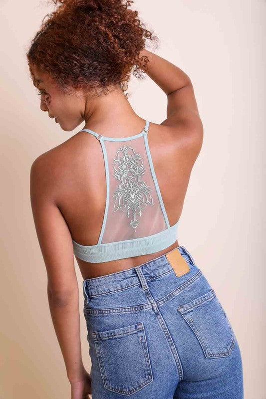 Person wearing a sheer top with floral embroidery and blue jeans on a beige background