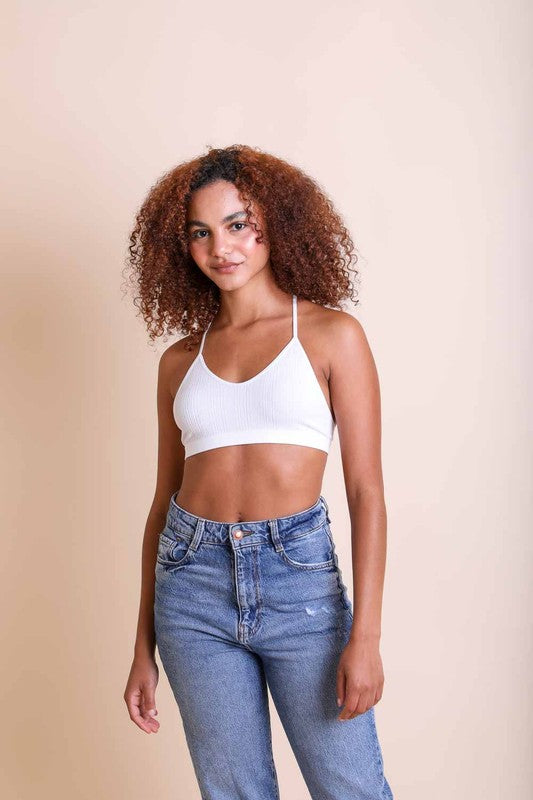 Woman wearing a white crop top and blue jeans against a beige background