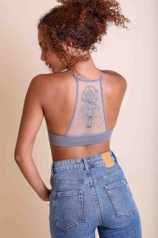 Person wearing a sheer blue top and jeans with a beige background