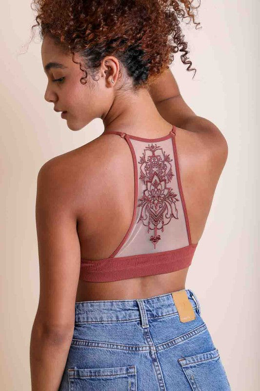 Person wearing a maroon sports bra with intricate back design and blue jeans on a beige background