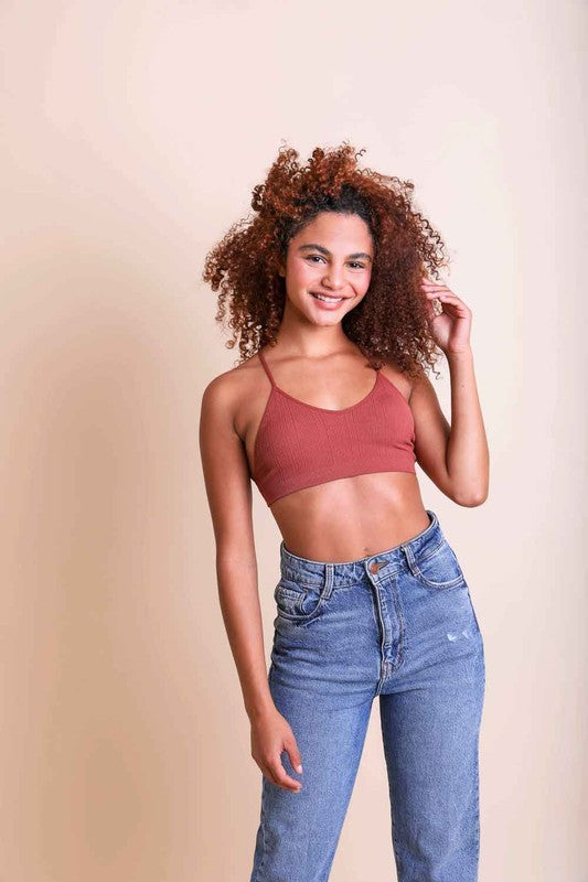 Woman wearing a red sports bra and blue jeans against a beige background