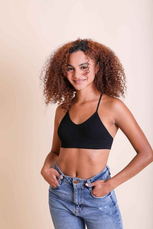 Woman wearing a black bralette and blue jeans against a beige background