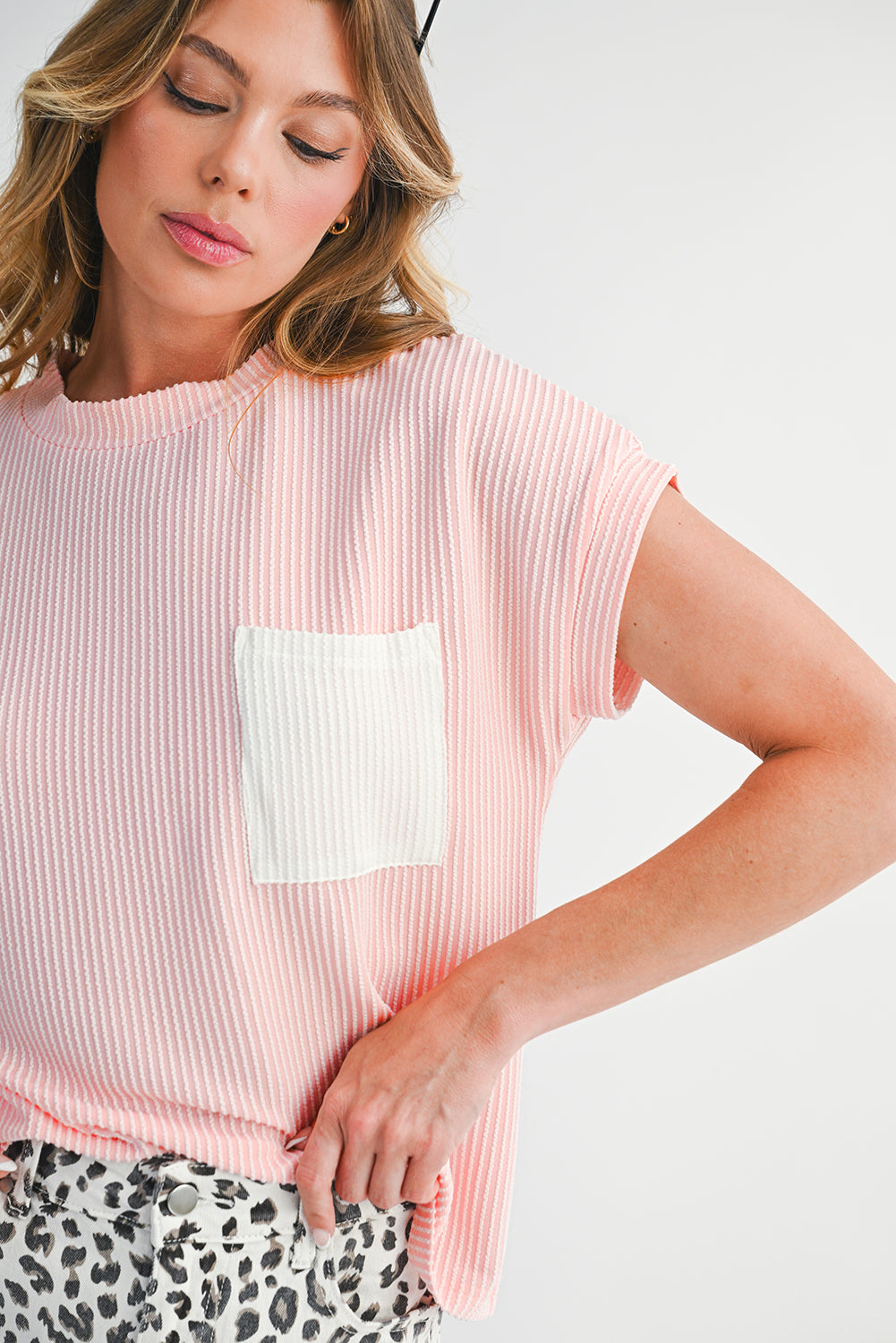 Woman wearing a pink ribbed top with a white pocket on a plain background