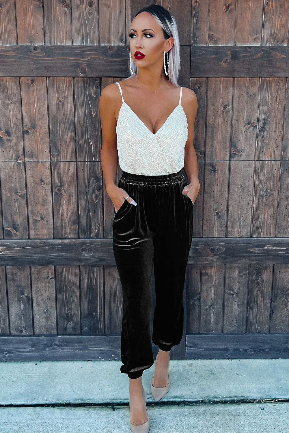 Woman wearing a white lace top and black pants against a wooden fence.