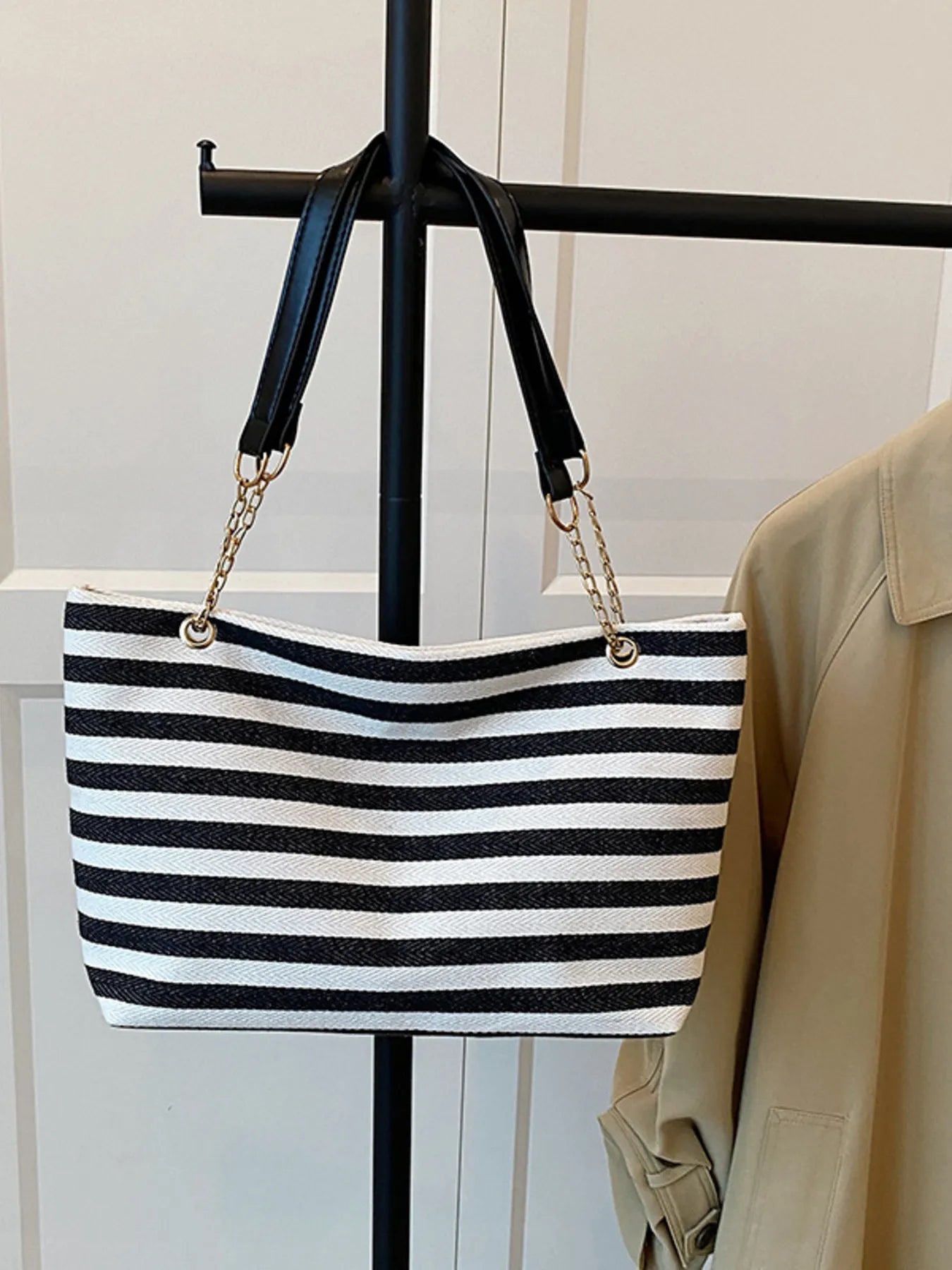 Black and white striped handbag with gold chain detail on a stand.