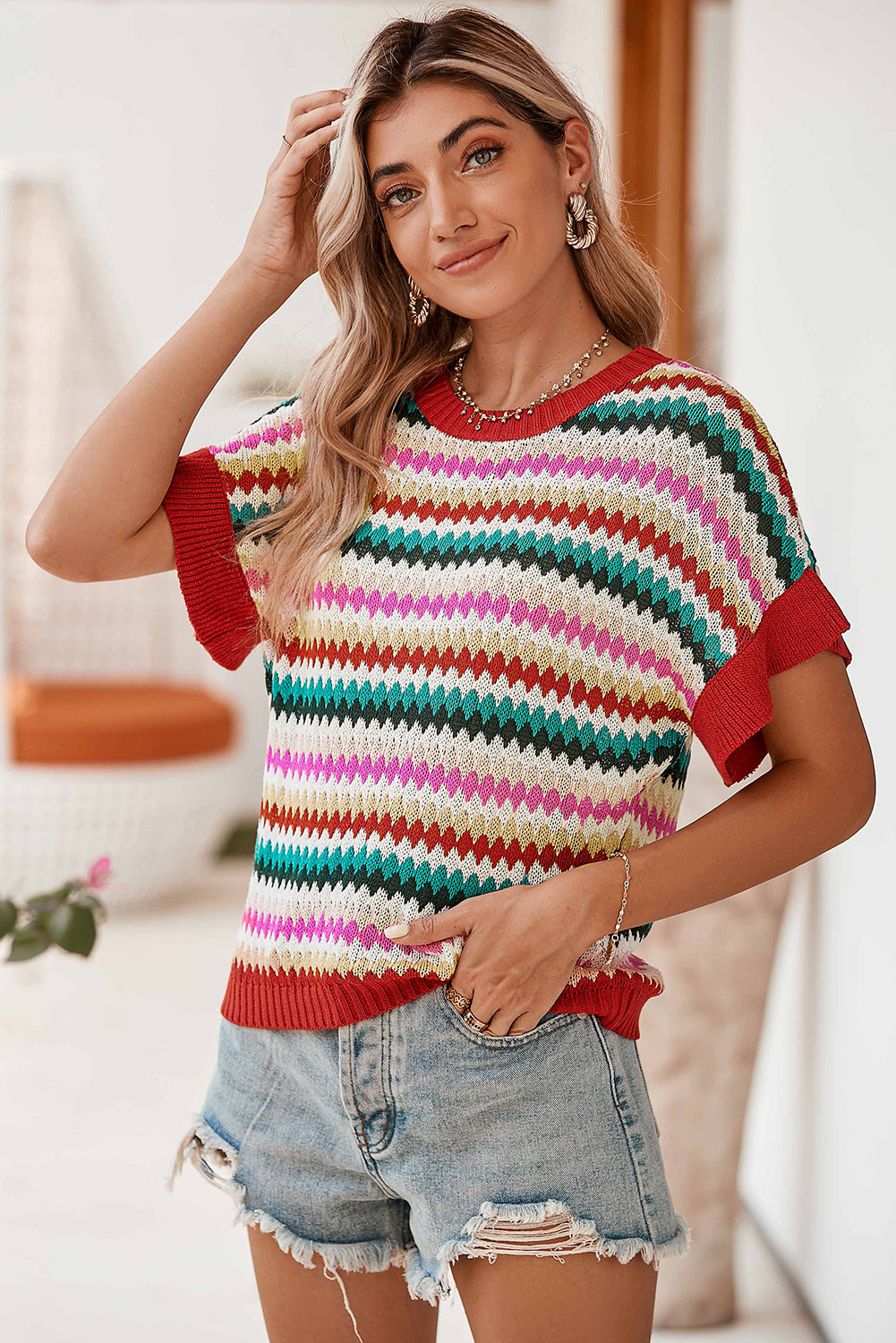 Woman wearing a colorful striped sweater and denim shorts indoors.