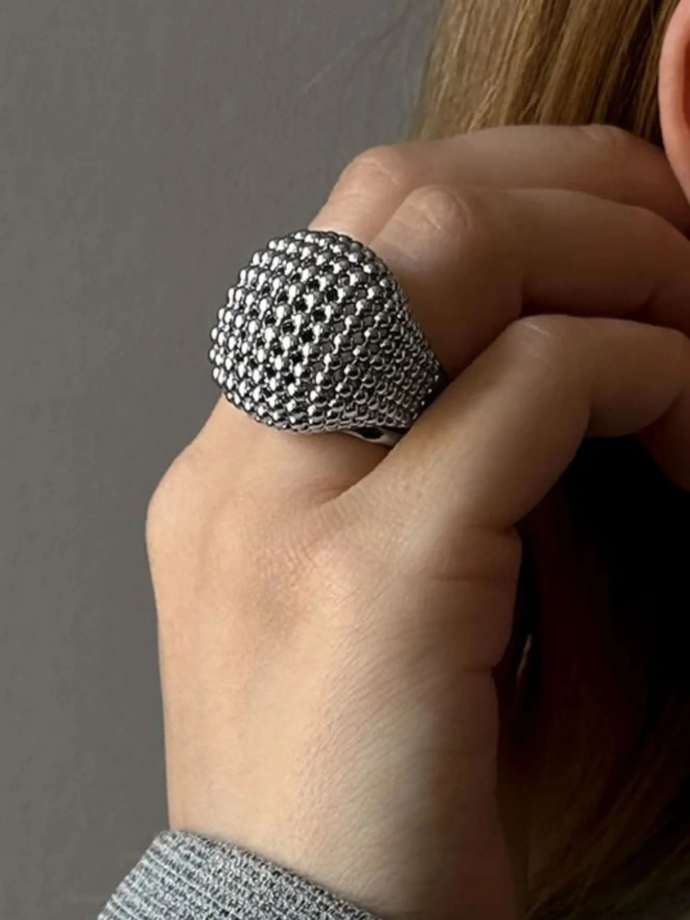 Hand wearing a textured silver ring against a neutral background