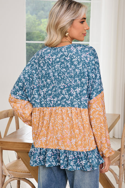 Woman wearing a floral blouse with a blue and yellow color scheme in a room with a window.