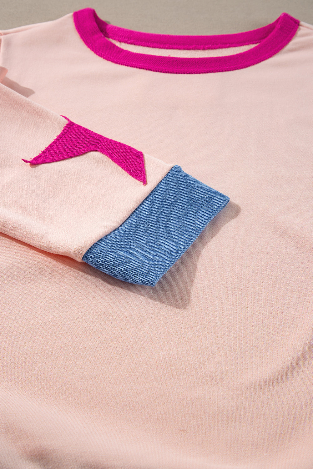 Close-up of a pink garment with blue trim and pink logo on a gray background