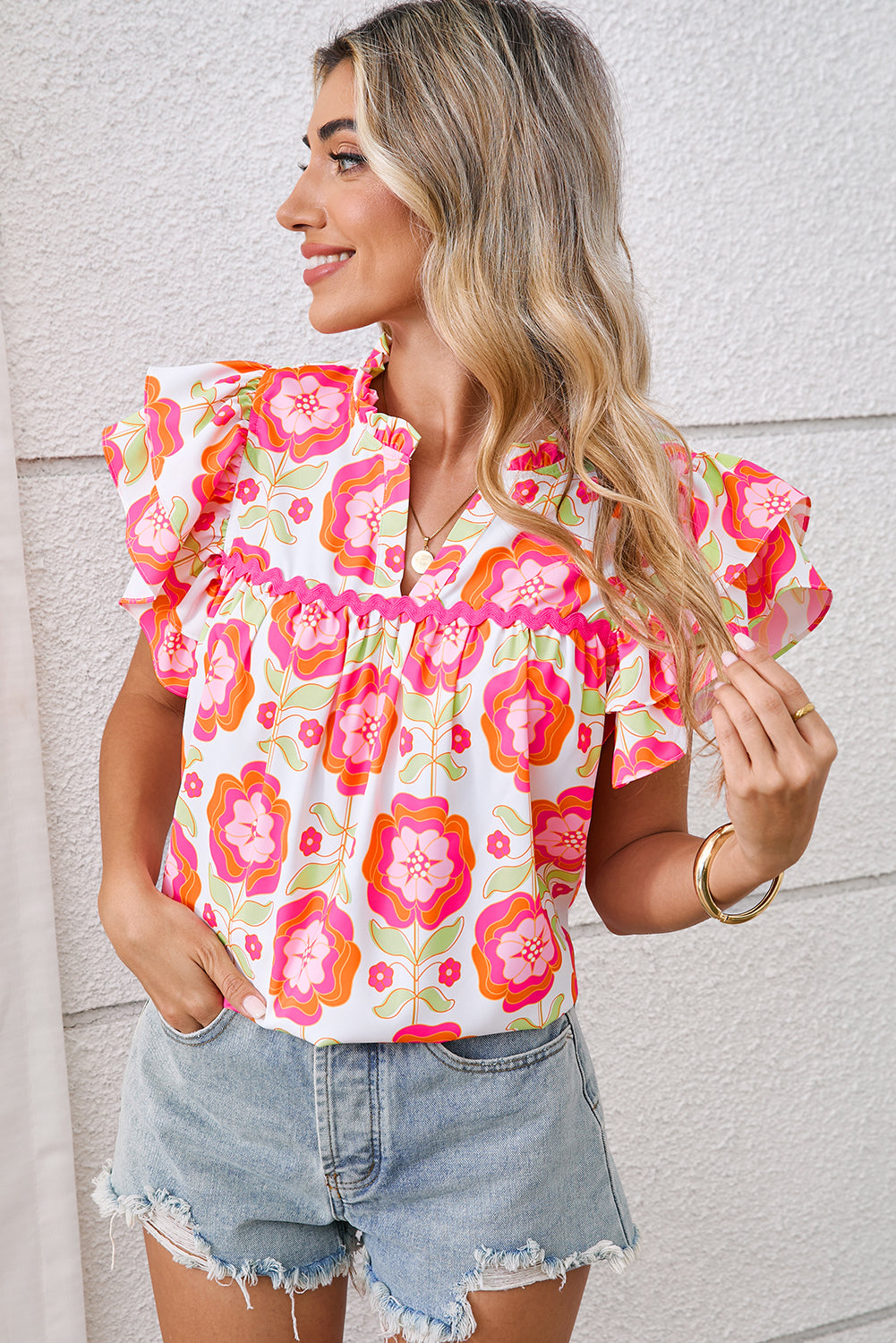 Woman wearing a colorful floral blouse and denim shorts against a light background