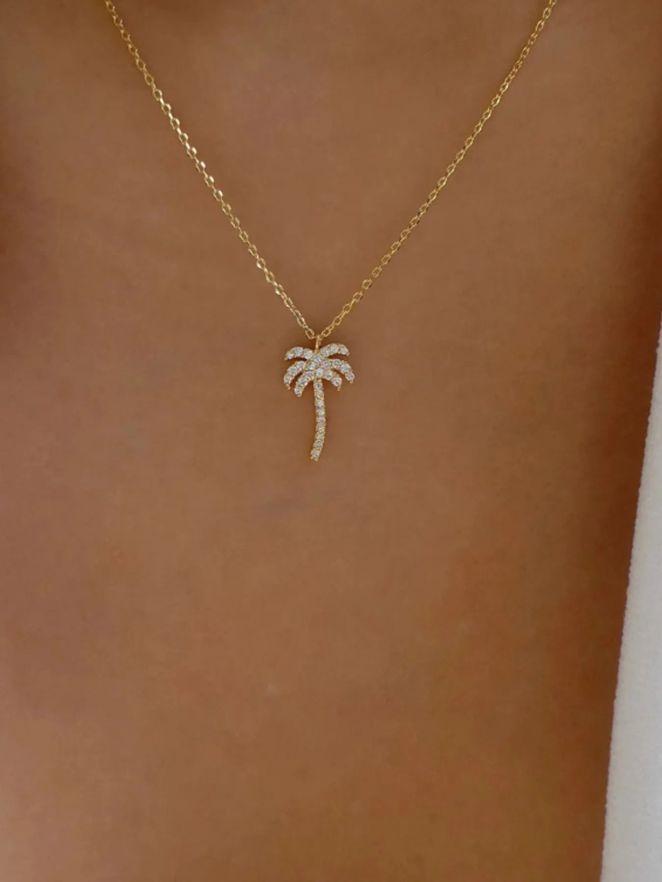 Gold necklace with a palm tree pendant on a person's neck