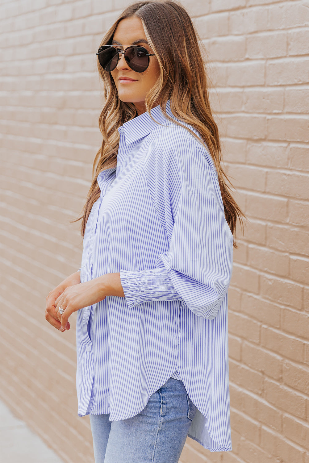 Woman wearing a blue and white striped shirt against a beige brick wall