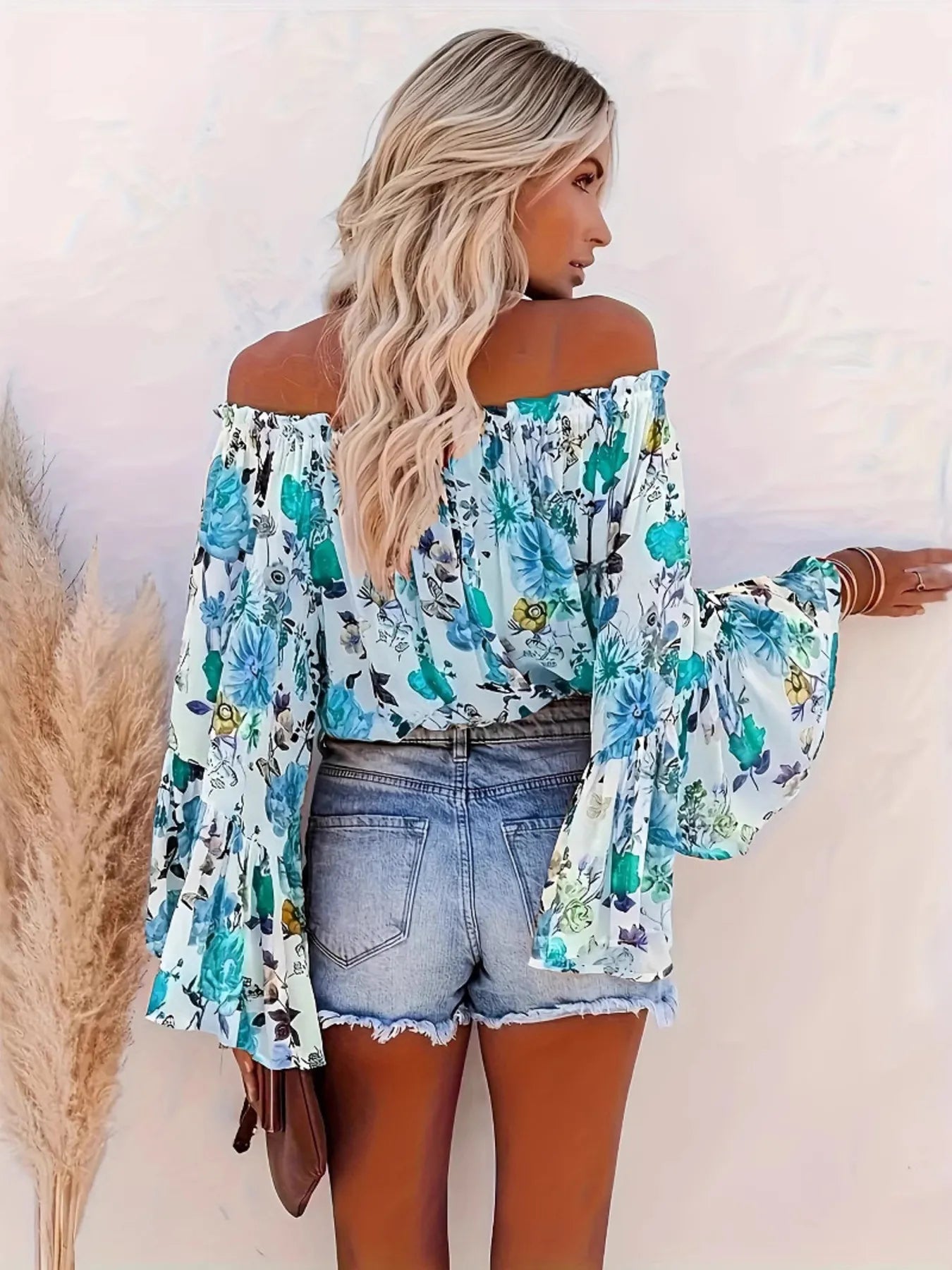 Woman wearing a floral off-shoulder top and denim shorts against a white background