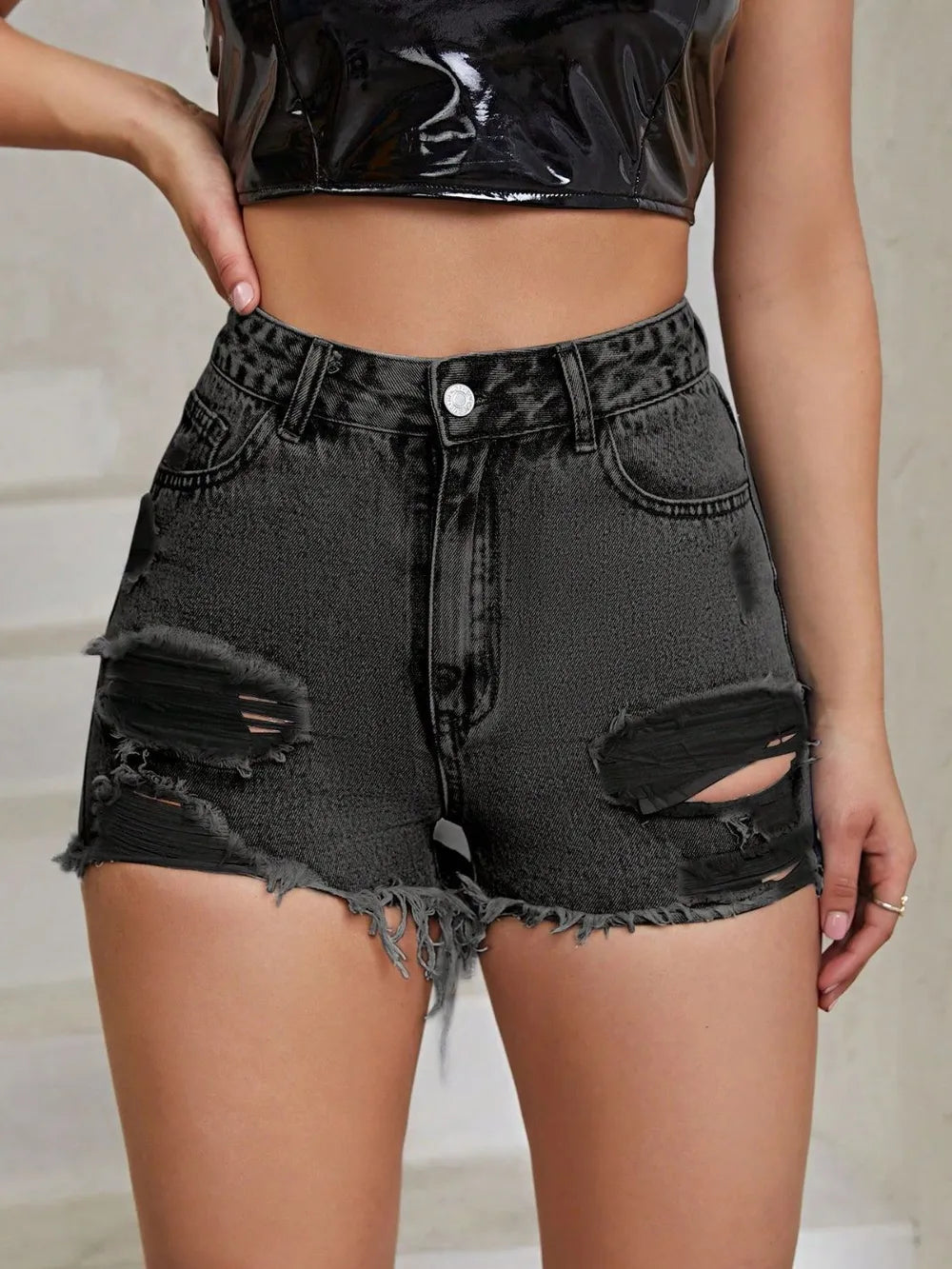 Person wearing black distressed denim shorts with a plain background