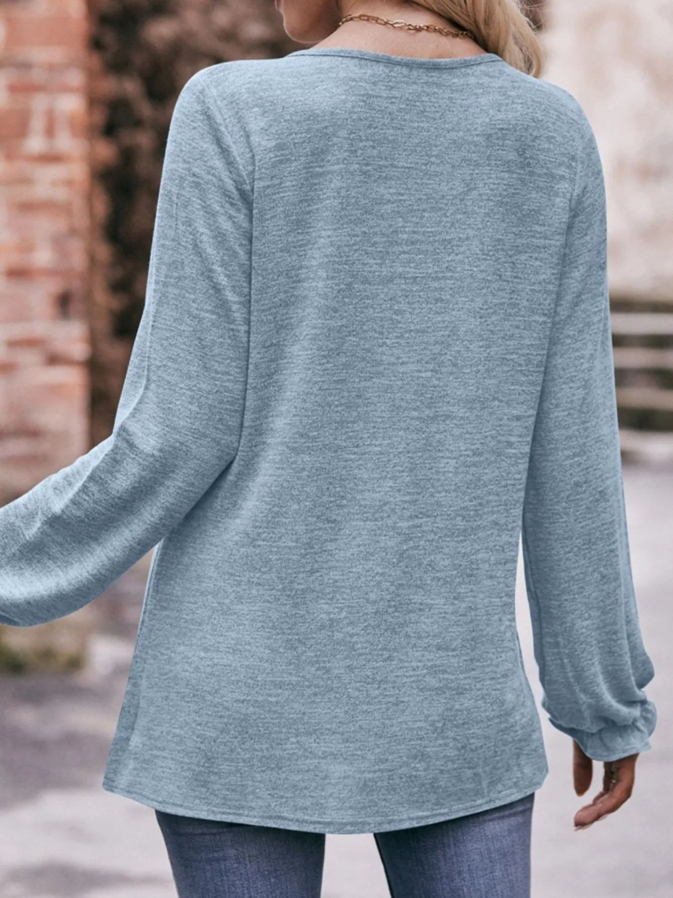 Person wearing a light blue long-sleeve top with a blurred background