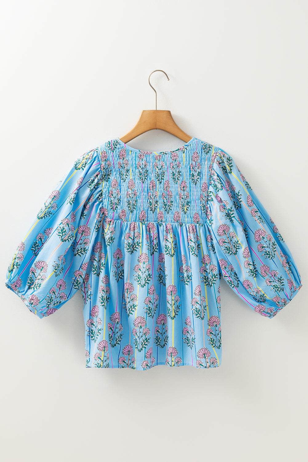 Floral blouse with balloon sleeves on a wooden hanger against a white background