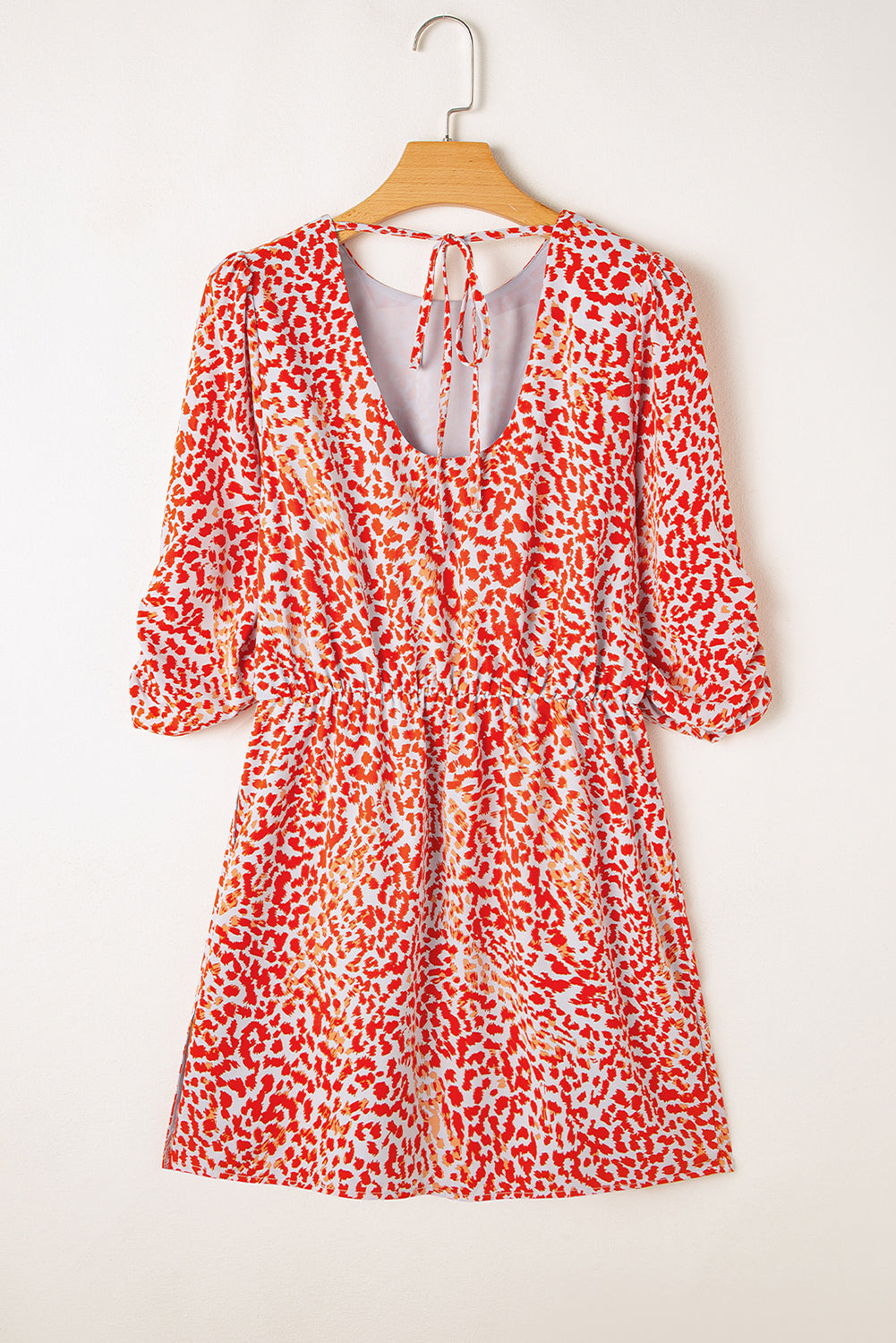 Red and white patterned dress on a wooden hanger against a white background