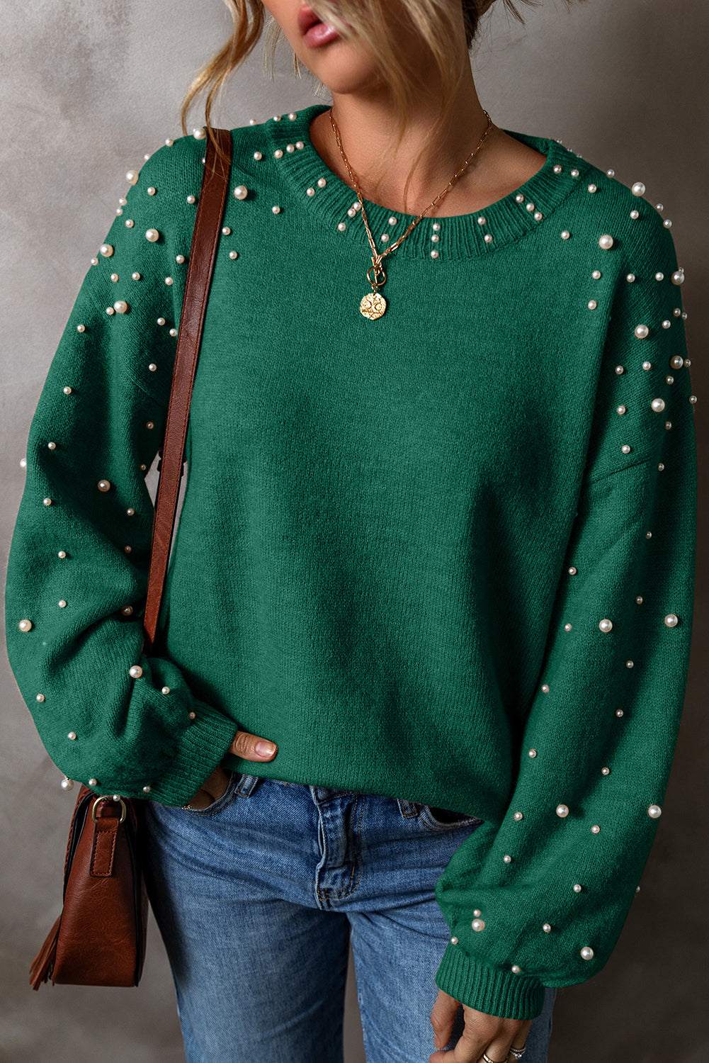 Green sweater with pearl embellishments worn by a person, against a neutral background