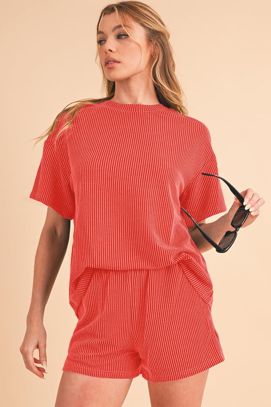 Woman wearing a red ribbed outfit holding sunglasses on a beige background