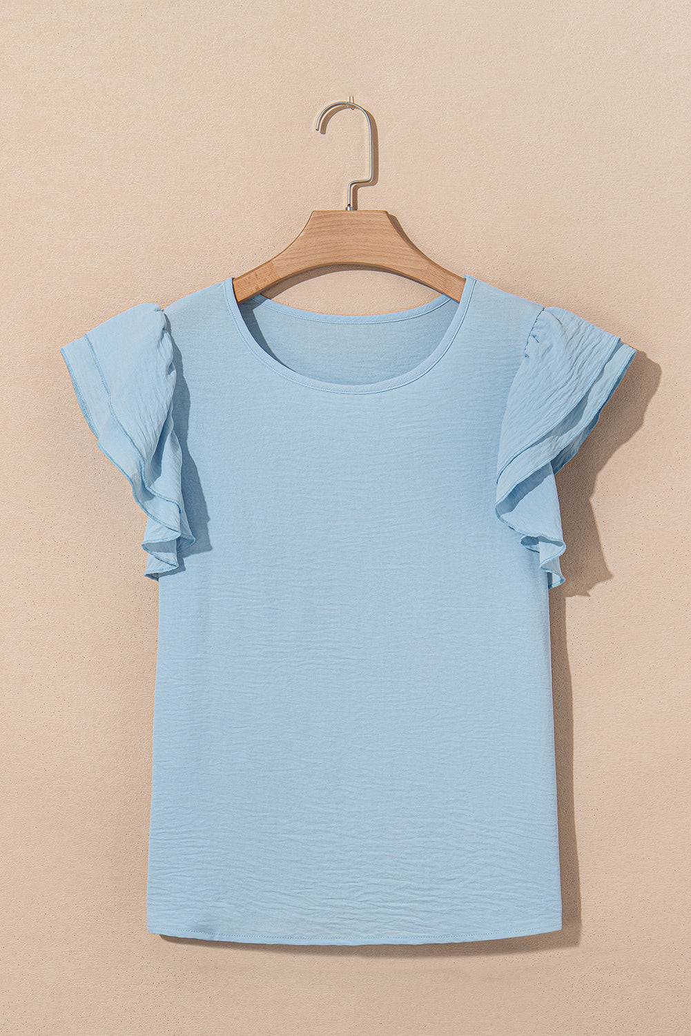 Light blue ruffled sleeve top on a wooden hanger against a beige background