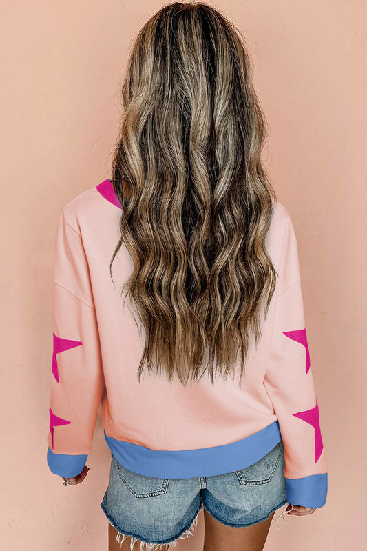Person wearing a pink sweater with star designs and denim shorts on a beige background
