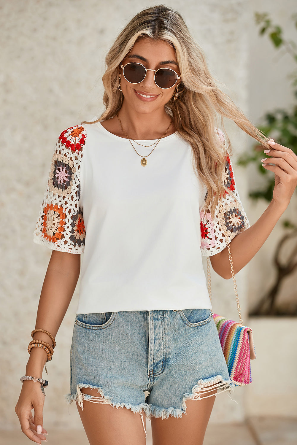 Woman wearing a white top with colorful sleeves and denim shorts, holding a colorful bag.