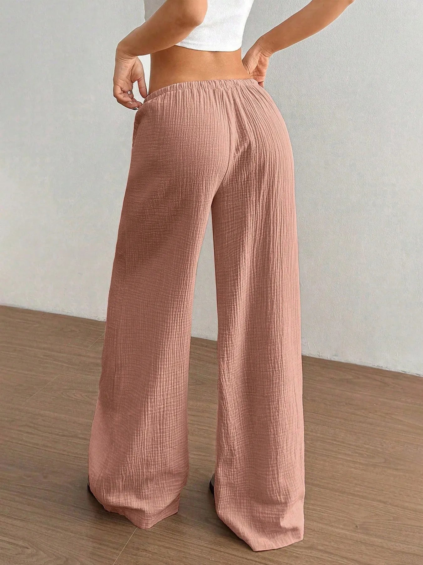 Person wearing pink corduroy pants on a wooden floor with a white wall background
