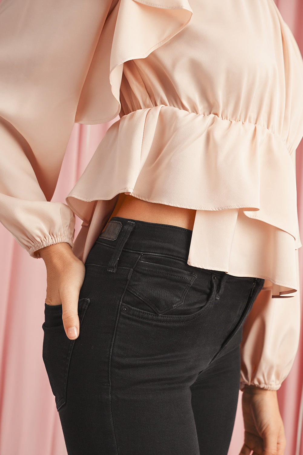 Person wearing a light pink blouse and black pants against a pink background