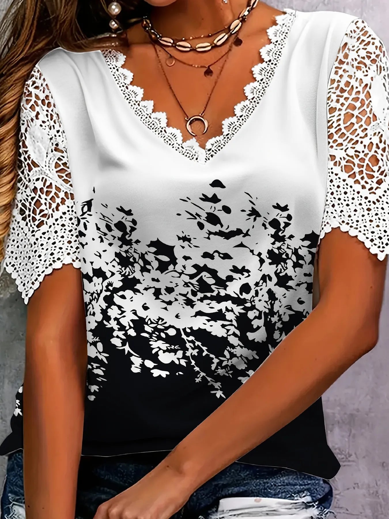 White blouse with black floral pattern and lace sleeves worn by a person.