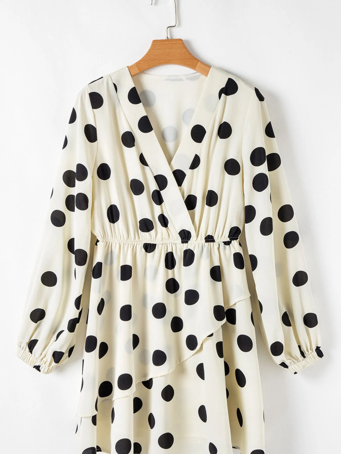 White dress with black polka dots on a hanger against a white background