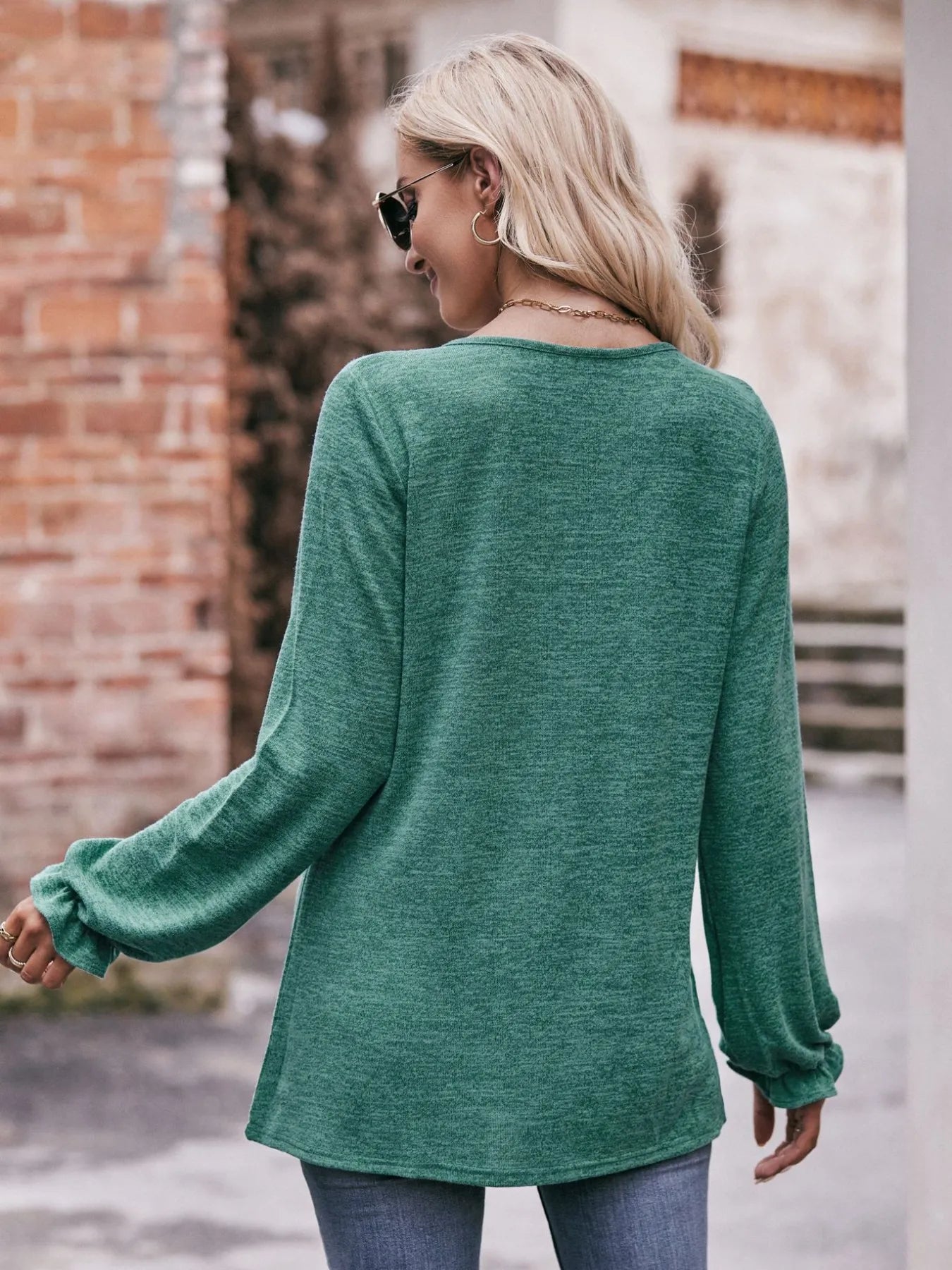 Woman wearing a green sweater with long sleeves in an urban setting.