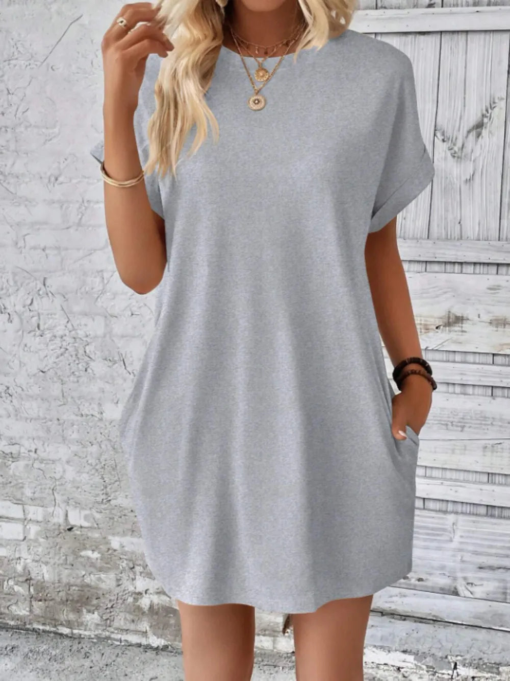 Woman wearing a gray dress against a textured white wall.