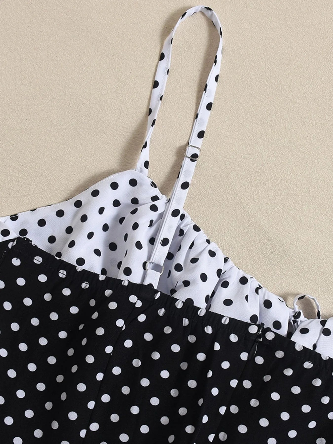 Black and white polka dot dress with thin straps on a beige background