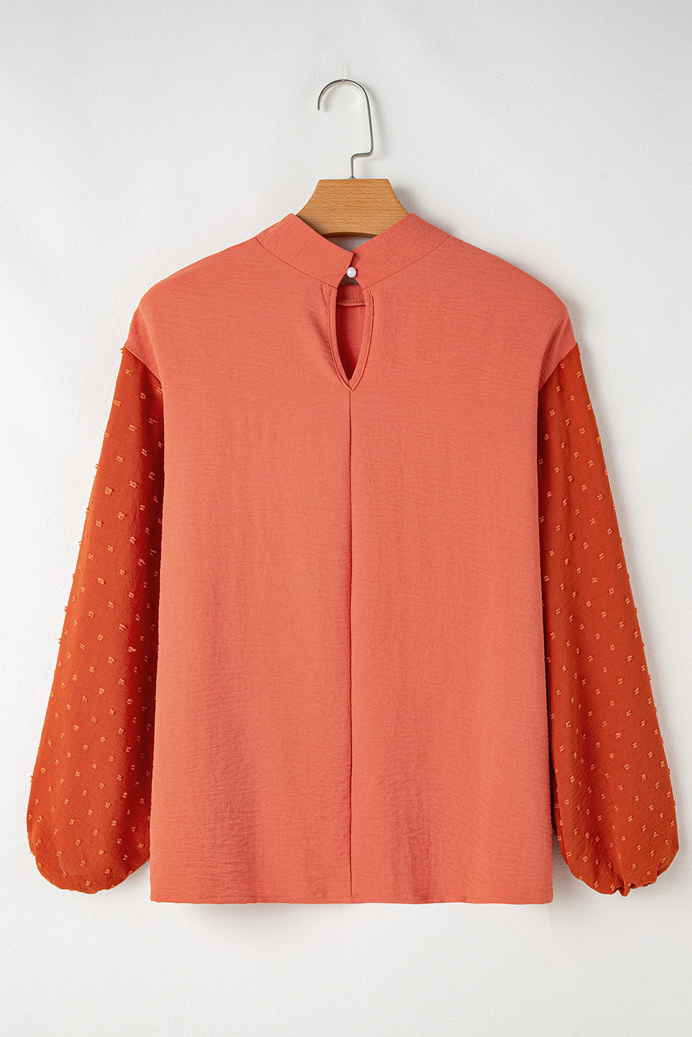 Coral-colored blouse with long sleeves on a hanger against a white background