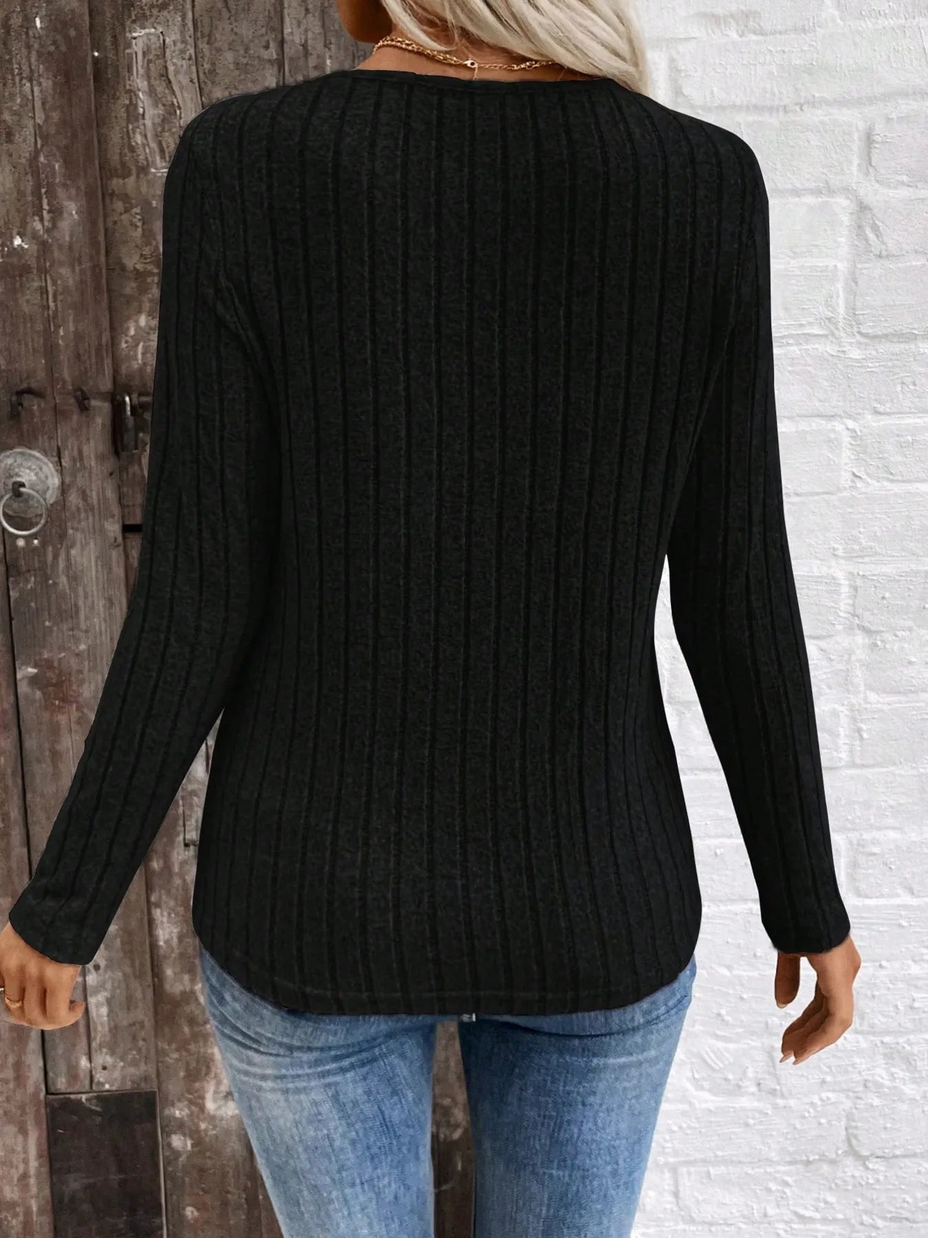 Person wearing a black sweater and blue jeans against a white brick wall.