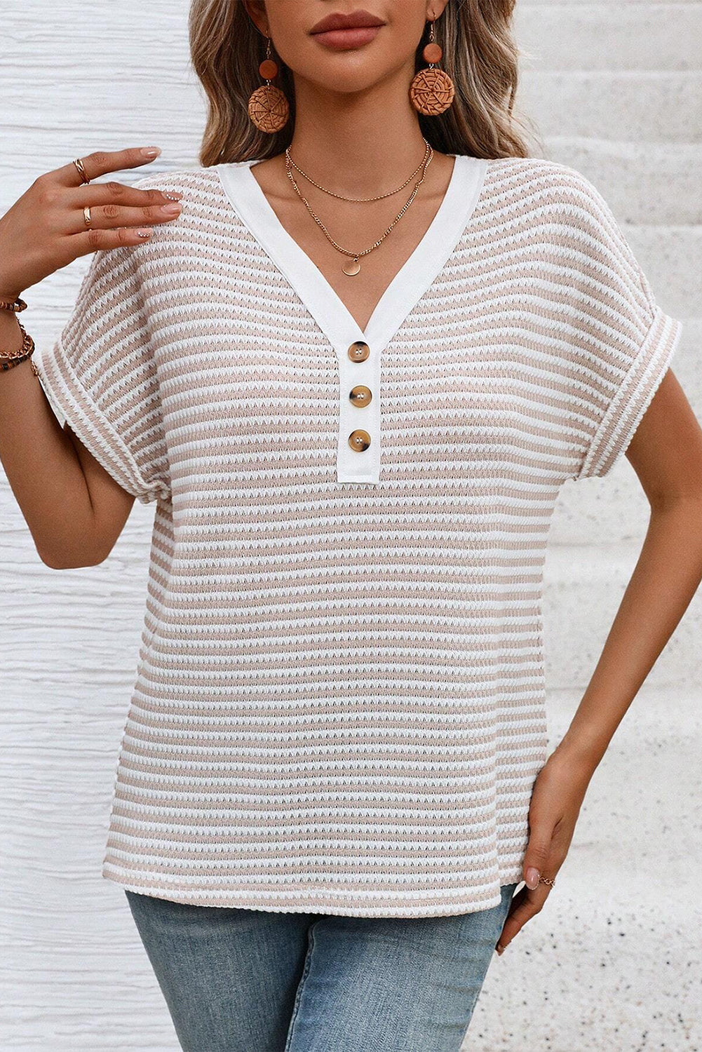 Woman wearing a textured white top with buttons and blue jeans against a light background