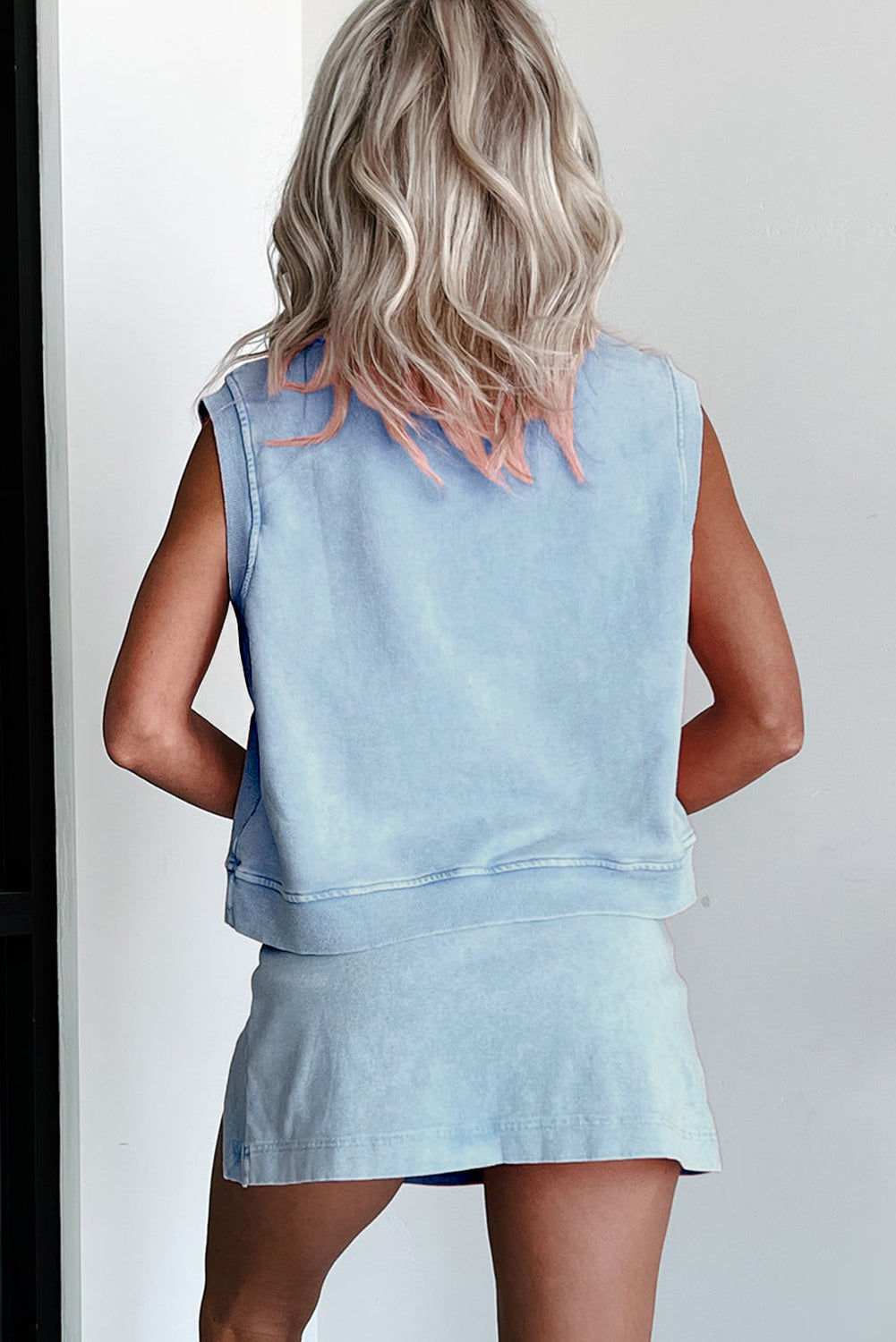 Person wearing a light blue sleeveless top and skirt set against a white background