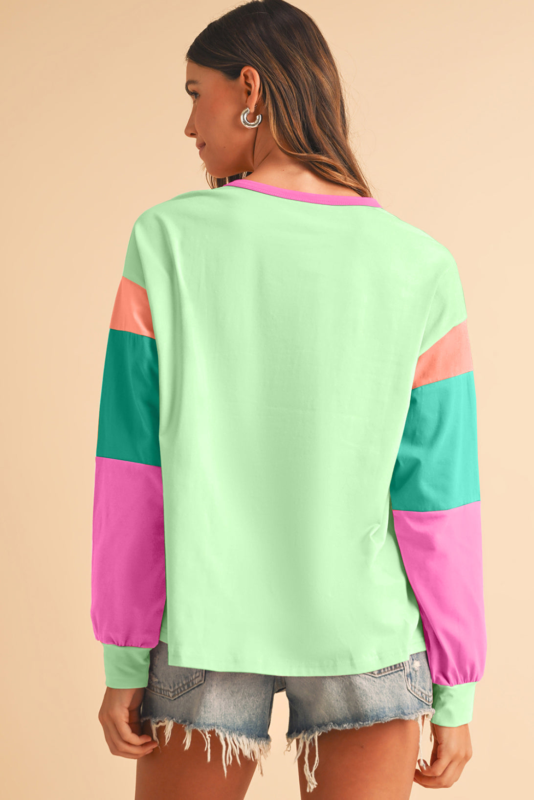 Person wearing a colorful sweater with green, pink, and teal sleeves on a beige background
