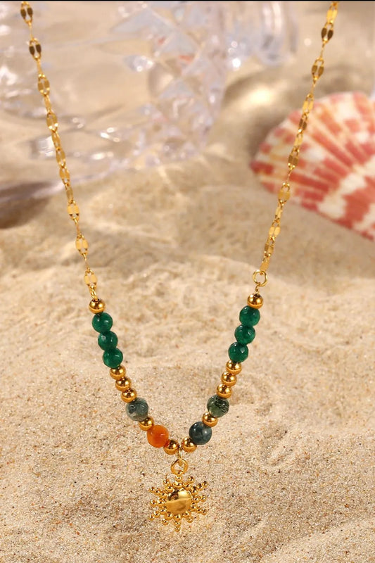 Necklace with green and orange beads and a gold charm on sand