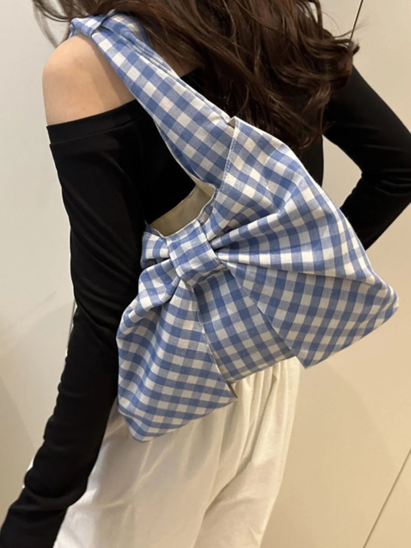 Person wearing a blue and white checkered scarf over a black top and white pants.