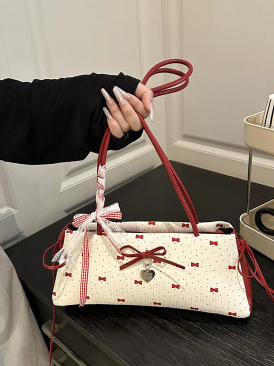 Handbag with red handles and bow design held by a person indoors.