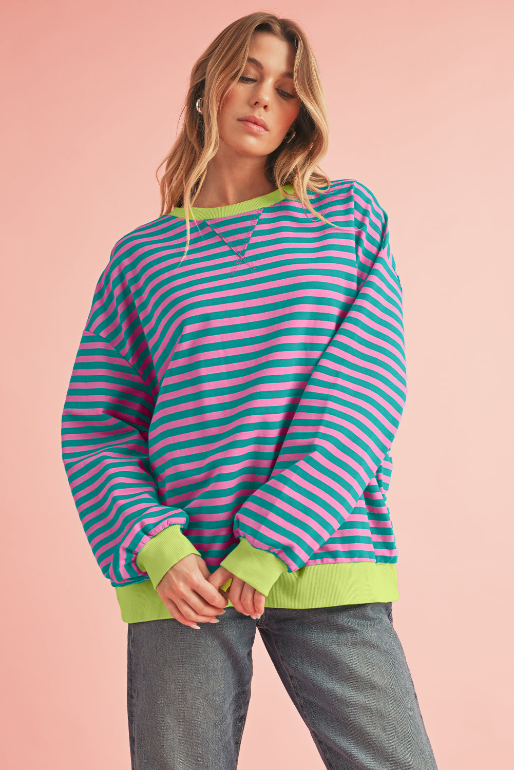 Woman wearing a striped sweater with green trim on a pink background